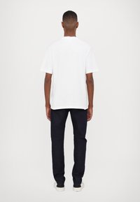 White cotton t-shirt with short sleeves, paired with dark blue jeans. The t-shirt has a relaxed fit and a plain design. White sneakers complete the look.