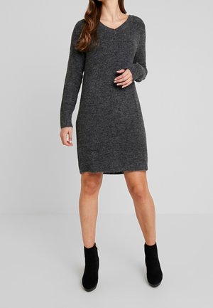 Abito maglione grigio carbone a maglia con maniche lunghe, scollo a V e orlo leggermente sfrangiato. Indossato con stivali neri alla caviglia.