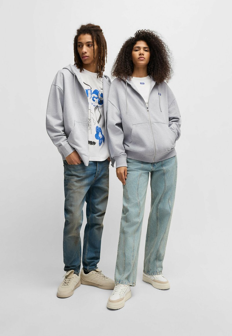Gray zip-up hoodie, graphic white t-shirt, light blue baggy jeans, neutral sneakers, featuring a relaxed fit and soft fabric.