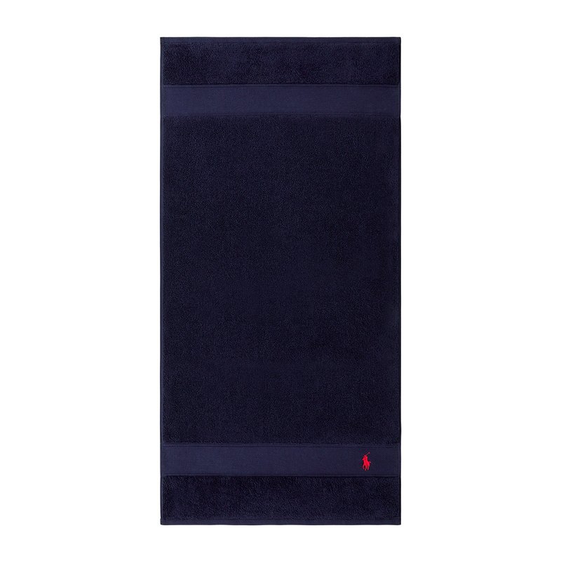 Πετσέτα σε ναυτικό μπλε χρώμα από περκάλι με λεί α υφή, διακοσμημένη με δύο οριζόντιες λωρίδες και ένα μικρό κόκκινο λογότυπο στο κάτω μέρος.