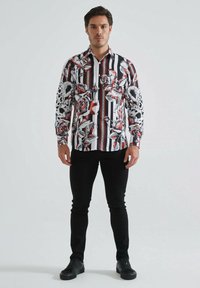 Chemise à manches longues avec un motif floral et ray�é en noir, rouge et blanc. Fabriquée en tissu lisse, avec une conception à boutons et un col.
