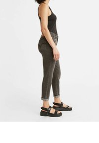 Top negro sin mangas, jeans de talle alto grises con puños enrollados y sandalias negras gruesas. Los jeans tienen detalles en los bolsillos traseros.