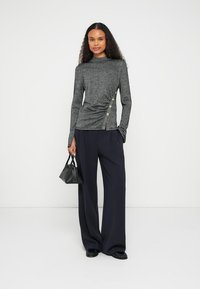 Gray long-sleeve top with a fitted silhouette, gathered side, and three gold buttons. Paired with wide-leg navy trousers and a small black handbag.