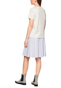 Light gray t-shirt paired with a pleated light purple skirt, showcasing vertical stripes. The model wears gray ankle boots with black accents.