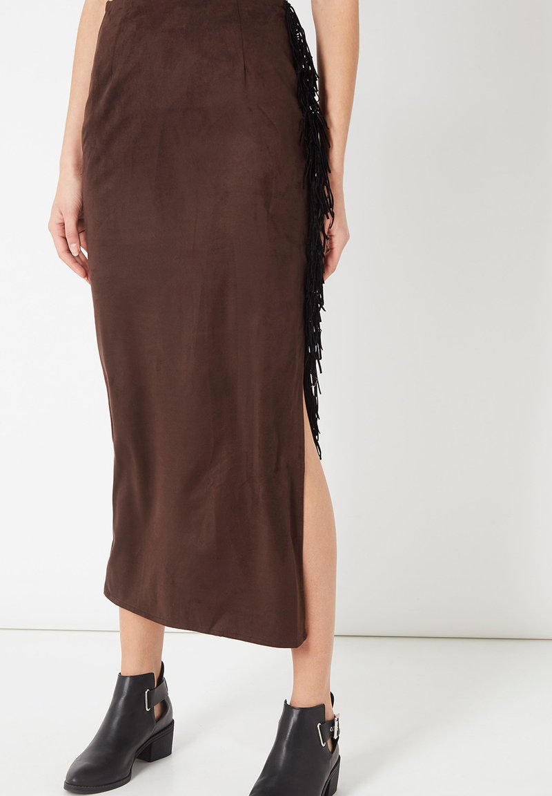 Falda midi marrón ajustada con detalle de flecos laterales y abertura, combinada con botines negros con cortes y hebillas.