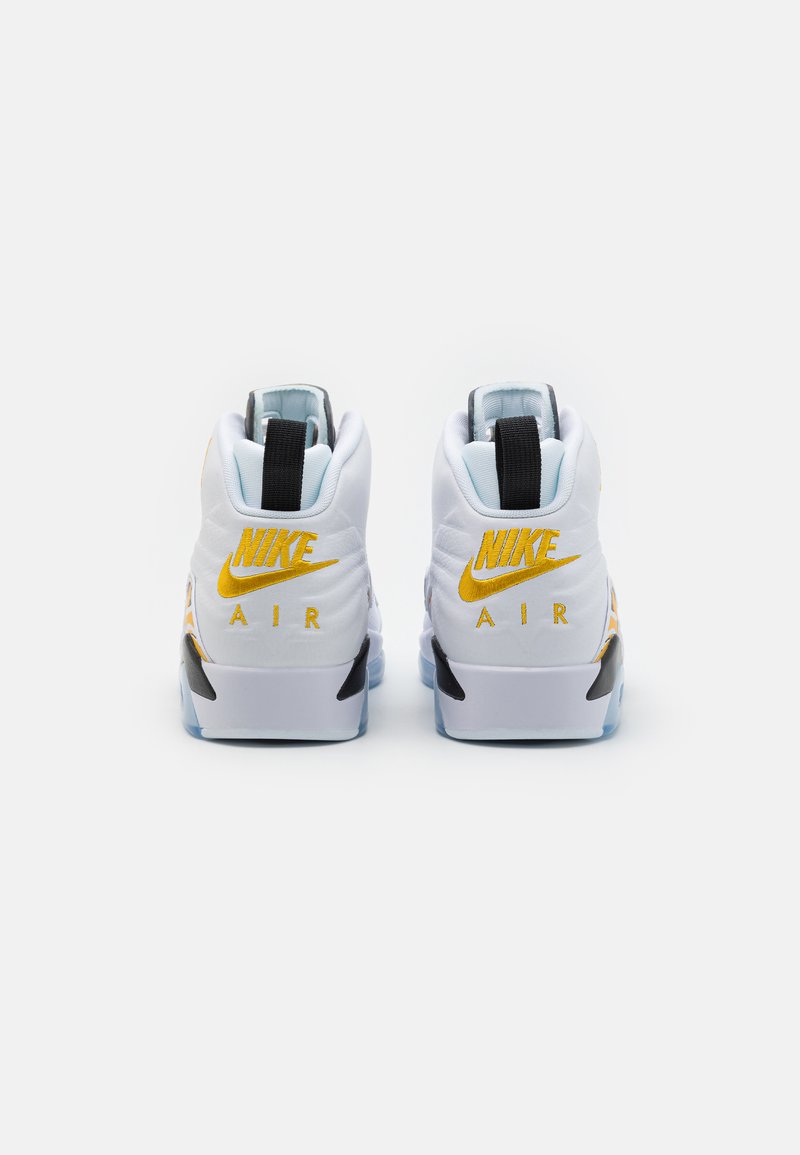 Białe sneakersy Nike Air z żółtym brandingiem, czarnymi akcentami i teksturowanym obcasem. Posiadają wyściełany kołnierz i przezroczystą podeszwę.