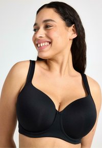 Svart underwire-bh med slätt tyg, helkapslade kupor, breda band och en sömlös design, med en central söm för struktur.