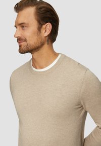 Bežs džemperis ar apaļu kakla izgriezumu, ribotām piedurknēm un smalku logo izšuvumu uz krūšu daļas. Mīksta tekstūra, pieguļošs dizains.