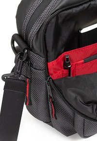 Borsa in tessuto nera e grigia con chiusura con zip, tasche interne rosse e hardware di fissaggio; presenta un esterno texturizzato e una tracolla regolabile.