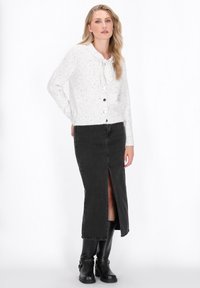 White, speckled knit cardigan with a tie neckline and buttons, paired with a high-slit black denim skirt and black knee-high boots.