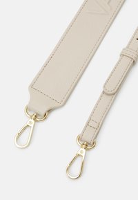 Cinturino in pelle beige con accessori in metallo dorato. Presenta una superficie testurizzata e due estremità con ganci per l'attacco. Design semplice e funzionale.