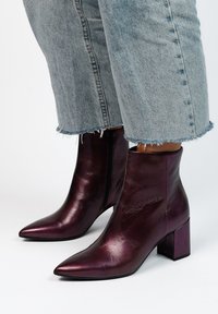 Bottines en cuir violet avec un orteil pointu, un talon carré et une fermeture éclair sur le côté. La finition texturée et l'apparence lisse renforcent le design.