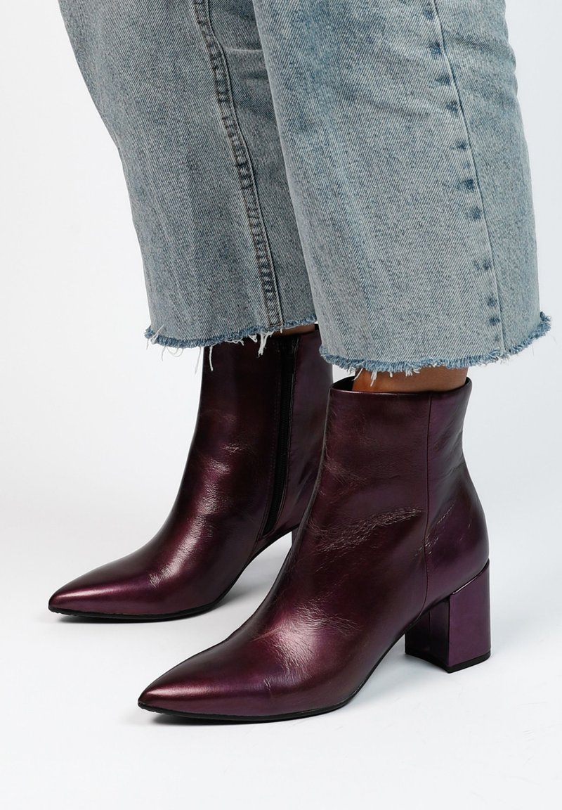 Bottines en cuir violet avec un orteil pointu, un talon carré et une fermeture éclair sur le côté. La finition texturée et l'apparence lisse renforcent le design.