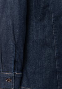 Dark denim shirt section featuring a button cuff, visible stitching, and a smooth texture with a slightly faded finish.