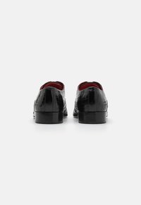 Scarpe in pelle nera con motivo coccodrillo, dalla superficie liscia, punta arrotondata e foderate di un rosso a contrasto. Presentano un tacco basso per maggiore stabilità.
