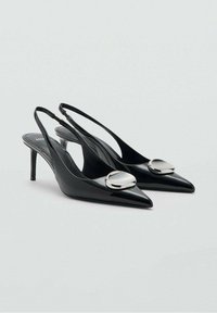 Tacones slingback de charol negro con punta afilada, con detalles metálicos redondos y tacones de aguja delgados. Textura suave y diseño elegante.