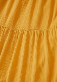 Tissu jaune doré avec des rayures texturées verticales et une couture froncée créant de subtils plis sur le matériau.