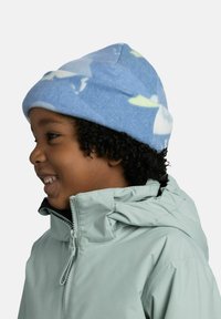 Light blue fleece hat with a layered design, featuring white and green abstract shapes. Worn by a child in a light gray jacket.