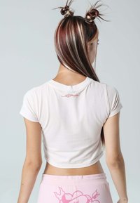 Lys pink crop top med korte ærmer, blød tekstur og rund halsudskæring, med et rødt broderet logo på ryggen.