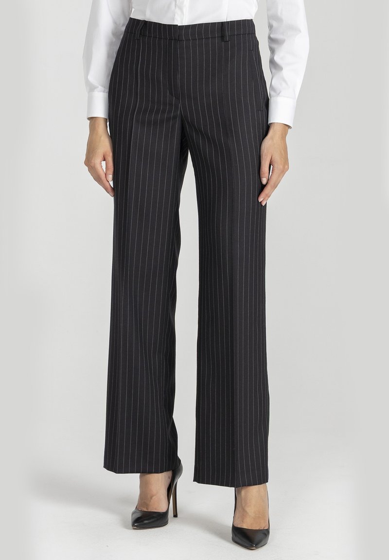 Czarne spodnie w prążki o luźnym kroju, z prostym przodem, kieszeniami bocznymi i gładką teksturą materiału. Połączone z czarnymi szpilkami.