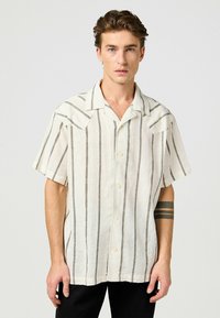 Camicia di lino a maniche corte color crema chiaro con strisce verticali grigio scuro, dotata di colletto e chiusura con bottoni.