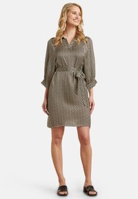 Schwarzes und weißes Kleid mit Zickzackmuster, einem Gürtel, langen Ärmeln und einem Kragen. Glatter Stoff, knielanges Design und lockere Passform.