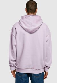 Lilac hoodie with a large hood, relaxed fit, and dropped shoulders. Soft cotton material with ribbed cuffs and hem. Worn with blue jeans.