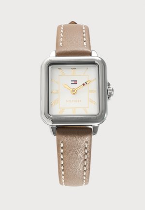 Strieborné štvorcové hodinky s béžovým koženým remienkom, zlatými rímskymi číslicami a logom Tommy Hilfiger na bielom ciferníku.