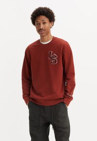Bordeaux sweatshirt met een ronde hals en witte afwerking, voorzien van een geborduurd "LS" logo op de borst en merkdetail op de mouw.