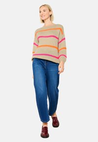 Beige gebreide trui met roze en oranje strepen, gecombineerd met blauwe rechte jeans en glanzende kastanjebruine schoenen.