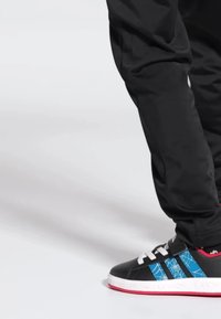 Svart sneaker med blå spindelnätsdesign på sidorna, vit sula och svarta snören. Bärs med svarta byxor som visar ankeldelen.