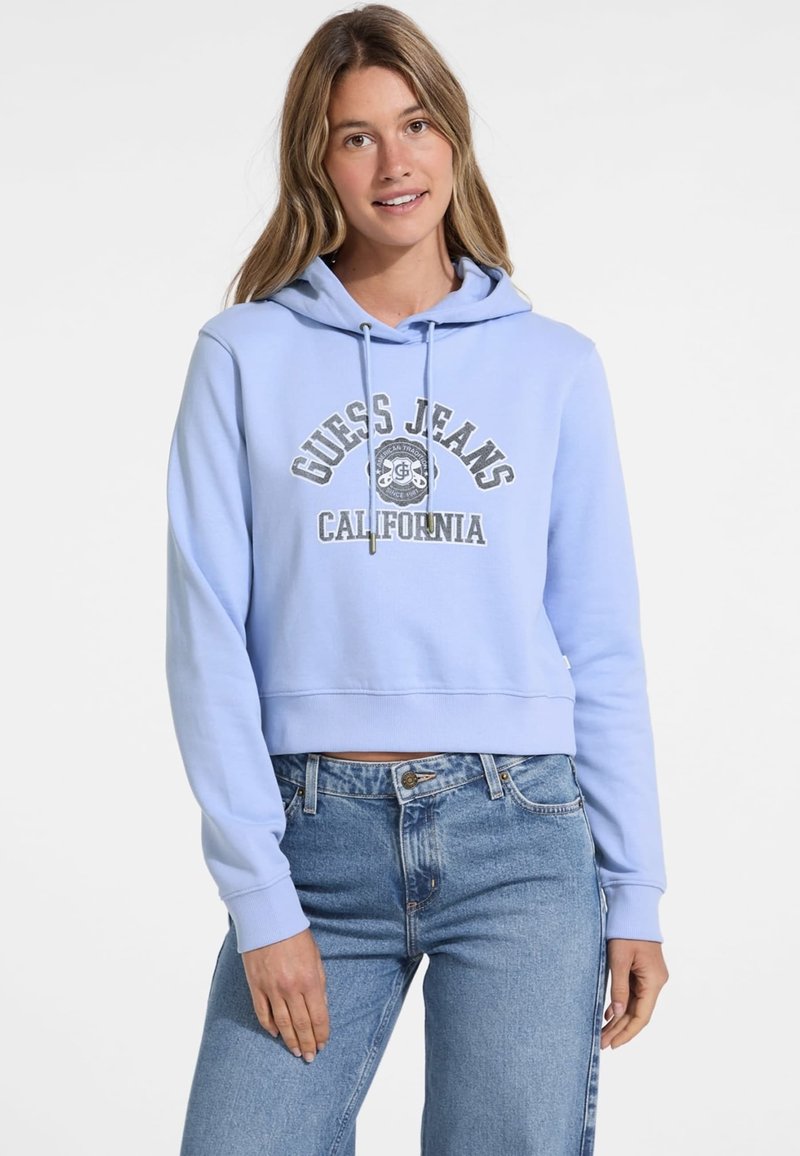 Cropped hoodie azzurro chiaro con grafica grigia "Guess Jeans California", cappuccio con lacci e polsini a coste, abbinato a jeans in denim a vita alta.