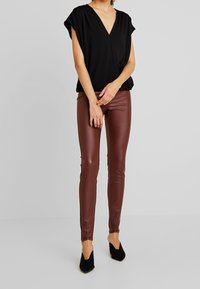 Top nero a V con maniche corte, abbinato a pantaloni attillati in ecopelle bordeaux lucida e scarpe con tacco nere.