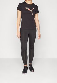 Camiseta negra con un logo colorido de Puma, combinada con leggings negros ajustados y zapatillas negras con detalles en rosa.