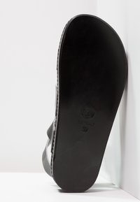 Černé gumové sandály s hladkou podešví, širokými pásky a jemnými detaily prošívání. Na spodní straně se nachází otisk loga a velikost 37.