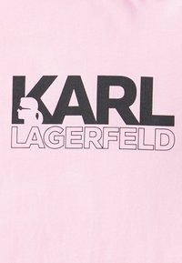 Camiseta rosa con texto negro en negrita que dice "KARL LAGERFELD," con un perfil en silueta y un estilo de diseño gráfico.