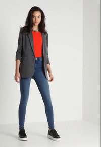 Szürke zakó piros felsőn, kék, skinny farmernadrággal és fekete tornacipővel párosítva. A zakón felhajtott ujjú és két elülső zsebe van.