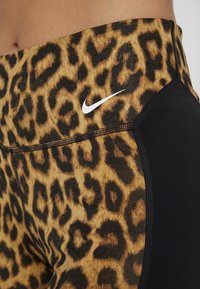 Legginsy Nike z wzorem panterki w brązie i czerni, o gładkiej fakturze, z czarnym bocznym panelem, na którym widnieje małe białe logo.