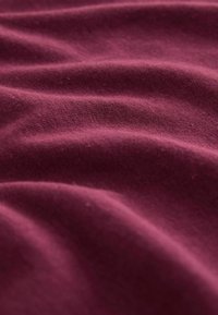 Dyb bordeaux-stof med en blød, struktureret overflade, der har subtile bølger og folder. Materialet fremstår let og strækbart.
