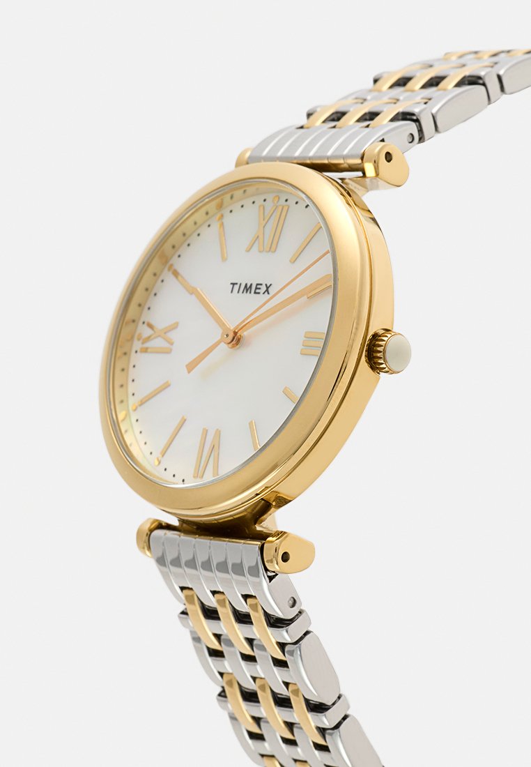 Zegarek na rękę Timex z złotą obręczą, białą tarczą, złotymi cyframi rzymskimi oraz dwutonową srebrno-złotą metalową bransoletą, wskazujący czas 2:10:50.