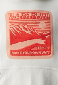 Sudadera blanca con un destacado bloque de logotipo bordado en rojo que presenta montañas, un sol y el texto "NAPAPIJRI" y "HAZ TU PROPIO CAMINO" debajo.