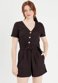 Combinaison noire courte avec un décolleté en V, des manches courtes, des détails de boutons sur le devant et une taille ceinturée. Le tissu semble lisse avec une coupe structurée.