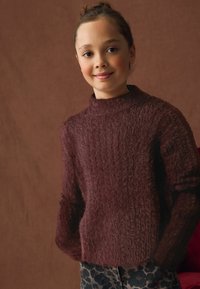 Vinröd stickad tröja med hög hals och ribbat mönster. Kombinerad med jeans i leopardmönster, vilket ger en avslappnad och mysig look.