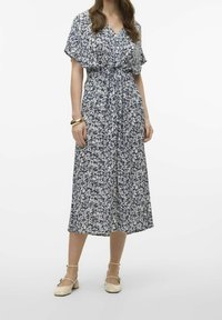 Květinové midi šaty s námořnicko-modrým a bílým vzorem, lehký materiál, výstřih do V a pas na šn urkování. Kombinováno se světle zbarvenými botami.
