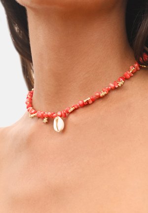 Collier de perles rouges avec accents dorés et pendentif en coquillage, composé de perles aux formes irrégulières rappelant le corail. Design texturé et en couches.