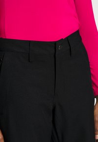 Black pants featuring a smooth texture, straight design, front pockets, and a button closure, paired with a bright pink top.