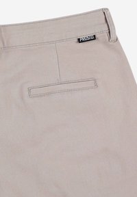 Beżowe spodnie o gładkiej strukturze, z tylną kieszenią o poziomym otwarciu oraz małą czarną metką z napisem "PROST."