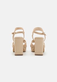 Beige platform heels with a block heel, suede straps around the ankle, and an adjustable buckle, featuring a smooth, glossy heel finish.