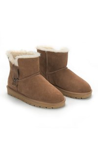 Botines de ante marrón con forro de pelo sintético, punta redondeada y suela de goma plana. Presenta una correa ajustable con detalles metálicos.