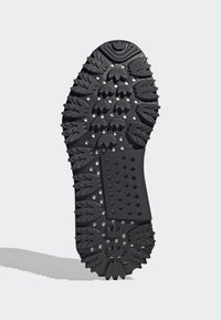 Black rubber shoe sole featuring a patterned grip with raised accents and a textured rectangular area with circular perforations.